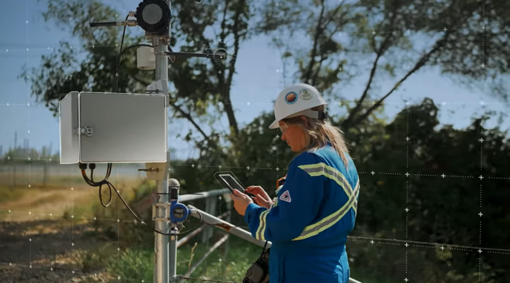 A woman in a blue vest and construction hat checks an air quality monitor.